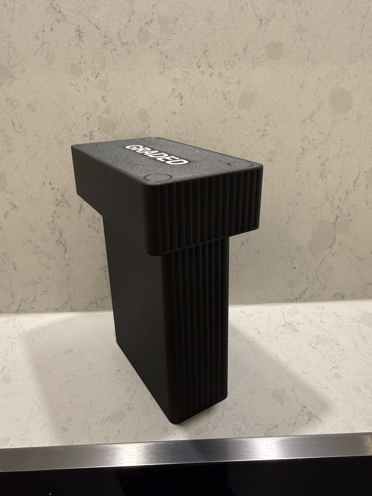 Angled photo of the real printed Formada3D graded card display case, closed, with GRADED engraved and painted on the lid, on a kitchen counter